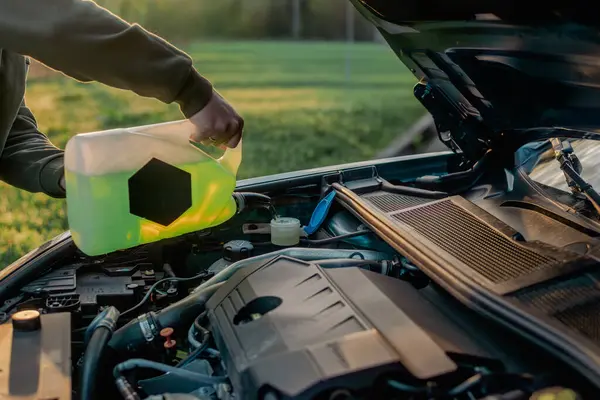 Açık kaputun altındaki araba deposuna cam temizleme sıvısı dökülüyor.