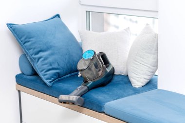 Pencerenin yanındaki oturma yerinde yastıklı elektrik süpürgesi var.