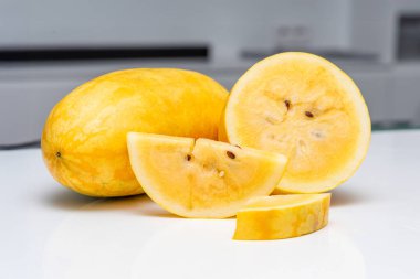 Yansıtıcı beyaz yüzeyde sarı karpuz dilimi ve arka planda tüm meyve