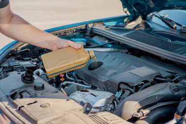 Bir arabanın motoruna motor yağı döken birinin yakın çekimi. Araç bakımı, yağ değişimi, otomotiv bakımı ve araba servisi kavramı.