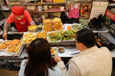 SEOUL, Güney Kore - 7 Nisan 2023: İnsanlar Güney Kore 'nin Jongno bölgesindeki Gwangjang Market' te bindaetteok krepleri yiyorlar.