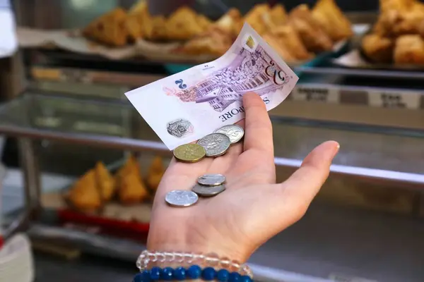 Stock image Hand holding Singapore dollars paper money with fast food snacks in background.