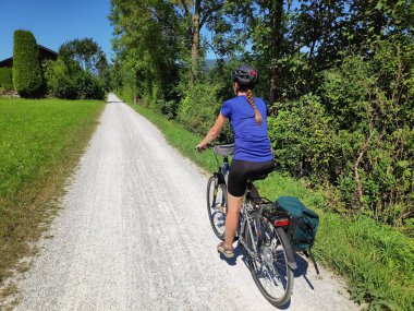 Avusturya 'da Tauernradweg üzerinde Salzburg yakınlarındaki Salzach nehri boyunca kask takan kadın bisikletçi..