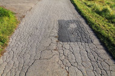 Damaged and patched local street in Chrzanow, Poland. Road maintenance concept. clipart