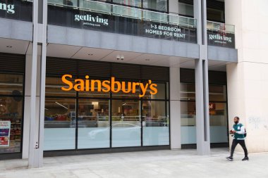 LONDON, İngiltere - 8 Temmuz 2024: Londra 'daki Sainsbury süpermarketinin önünden geçen kişi.