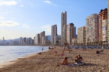 BENIDORM, İspanya - 7 Nisan 2025: İnsanlar güneşli bir günde İspanya 'nın Benidorm kentindeki Levante plajında öğleden sonralarını geçirirler.
