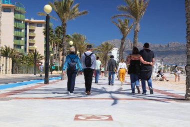 EL ALBIR, SPAIN - 9 Nisan 2025: İnsanlar İspanya 'nın Alicante Eyaleti Alfaz del Pi belediyesinde bir tatil köyü olan El Albir' de Passeig de las Estreles plaj bulvarı boyunca yürüyorlar.