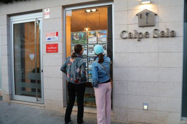 CALPE, İspanya - 6 Nisan 2025: Turistler, İspanya 'nın Alicante ilindeki Calp (Calp olarak da bilinir) kasabasında emlak acentesinin vitrinlerine bakıyorlar.