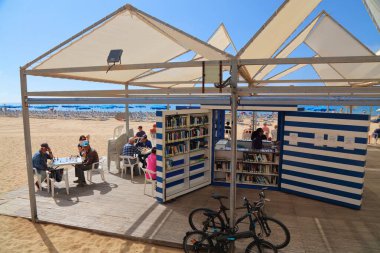 BENIDORM, SPAIN - 8 Nisan 2025: İnsanlar güneşli bir günde İspanya 'nın Benidorm kentindeki Levante plajının açık deniz kütüphanesini ve satranç kulübünü ziyaret ediyor.