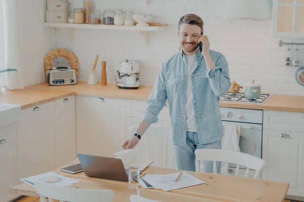 Przystojny Uśmiechnięty Brodaty Mężczyzna Ubraniu Pracujący Laptopie Stojący Przy Kuchennym — Zdjęcie stockowe