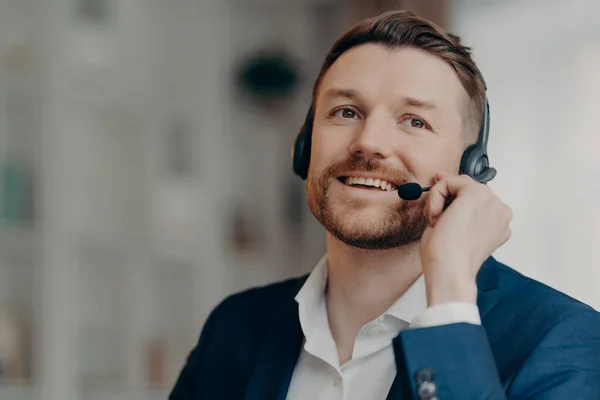 stock image Close up of happy office worker handsome male call center operator wearing headset and working in office, talking with client online with positive face expression, selective focus. Job and occupation