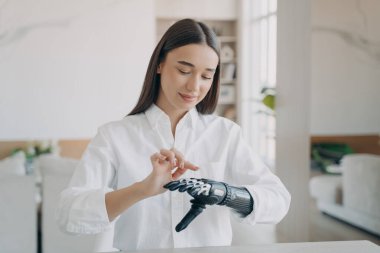 Young pretty disabled girl turns on her bionic prosthetic arm. Female training to use artificial robotic hand after limb loss. People with disabilities, medical high technologies concept. clipart