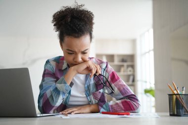 Bilgisayarla masa başında ders çalışan, sınava hazırlanan çift ırklı bir kız öğrenci. Düşünceli, yorgun, melez kız öğrenci ev ödevi yapıyor, evde öğrenim görüyor. Uzaklık eğitimi kavramı.