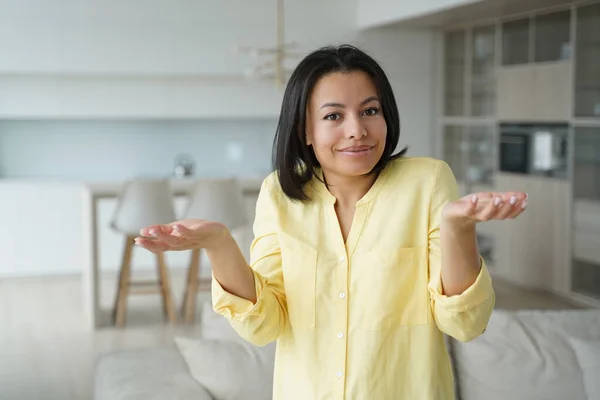 Confused young woman feels perplexity shrugging shoulders, raised palms, looking at camera at home. Puzzled unsure female homeowner housewife doesn\'t know answer. Dilemma, difficult choice.
