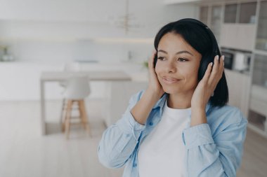 Kablosuz kulaklık takan, müzik, podcast ya da sesli kitap dinleyen mutlu bir kadın. Ses kalitesinin tadını çıkarıyor. Gülümseyen sakin kadın evde dinlenen, kulaklıkla olumlu yorumları dinler..