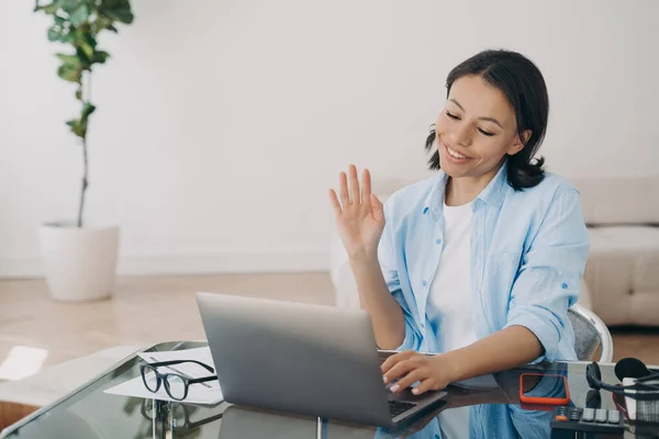 Happy woman working at laptop, waving hello, having video call, chatting with colleague or client at office. Smiling businesswoman teacher welcomes students to online seminar. E-learning, remote job.