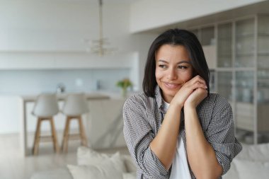 Gülümseyen genç bayan ev sahibi ya da kiracı evde dikilerek mutluluğu ve samimiyeti hissediyor. Mutlu esmer kadın ellerinin yanağında kıvrılmış, yeni evden memnun kalmış. İpotek, gayrimenkul satışı, taşınma..