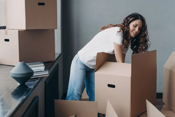 Hispanic woman unpack carton boxes with delivered things during relocation. Satisfied female tenant homeowner sorting belongings on moving day at new home. Real estate rental, mortgage.