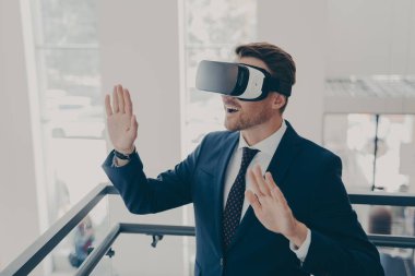 Yenilikçi iş teknolojileri iş başında. Takım elbiseli iş adamı ofiste sanal gerçeklik gözlüğü kullanıyor, iki eliyle havaya dokunuyor, ofis çalışanı 3D dijital dünyayla etkileşimde.