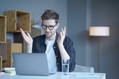 Kendinden emin Avrupalı işadamı, takım lideri dizüstü bilgisayarla video konferansı düzenliyor ev ofisinde oturup bilgisayarın ekranına bakarak elleriyle hareket ediyor.