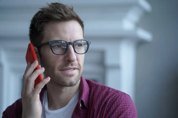 Close up portrait of confident thoughtful young German businessman in glasses having urgent conversation on mobile phone with main company office or copartner while working remotely from home