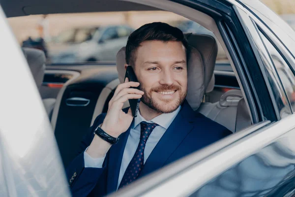 Happy company manager listening to his employee on topic of financial gain, hearing about high amount of profit possibilities, ready to go and make money, riding in back of luxury car