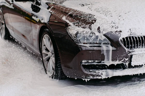 Lavaboda servis edilen siyah arabanın fotoğrafı. Araba yıkamada sabunla kaplı kirli bir otomobil. Profesyonel araba yıkama. Araç temizleme