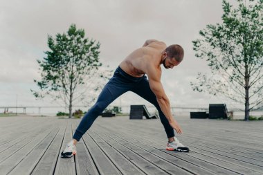 Sportif güdümlü yakışıklı adam eğilir ve spor egzersizleri yapar, dışarıda poz verir ve spor yapmakla meşgul olur. Kararlı gömleksiz adam spor ayakkabı giyer, parkta sabah antrenmanı yapar. Sağlıklı yaşam tarzı kavramı