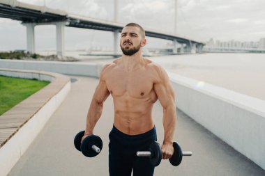 Uzakta yoğunlaşmış kaslı vücut geliştirici güçlü vücut kaslarına sahiptir güçlü kaslar halterleri tutar ve köprü ile nehir kenarında duran kaslar için egzersiz yapar. Sağlıklı yaşam tarzı ve spor anlayışı