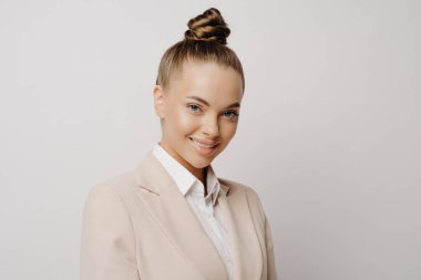 Klasik giyinmiş güzel bir kadın menajer büyüleyici bir gülümseme ve kendine güveni olan bir bakışla ışık arka planının yanında duruyor. Başarılı iş adamları