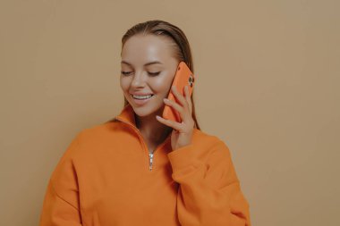 Isolated studio shot of happy smiling woman talking on mobile phone with best friend or family member, sharing last news via cellphone, female enjoying pleasant fun call conversation
