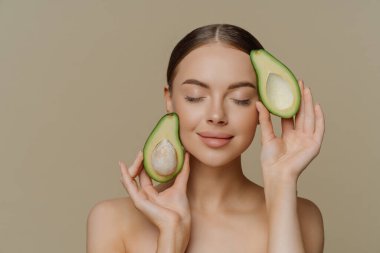 Sağlıklı bir kadının portresi gözlerini kapalı tutar. Kozmetik ürünler için temiz cilt bakımı yapılır. Güzellik prosedürleri bej duvarın üzerinde çıplak omuzlarla yapılır.