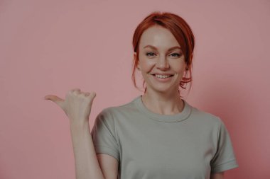 Yüzünde mutlu bir ifade olan neşeli kızıl saçlı kadının yatay görüntüsü boş fotokopi alanını işaret ediyor, reklam yaparken başparmağıyla işaret eden kadın. Reklam kavramı