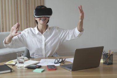 İş yerinde sanal gerçeklik gözlüğü kullanırken elini havaya kaldıran neşeli genç bir iş kadını, VR kulaklığı takmış kadın çalışan, yenilikçi aletleri iş için test ediyor. 3d görselleştirme kavramı