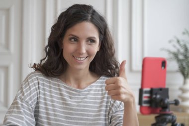 Neşeli İtalyan kadın blogcu etkileyicisi akıllı telefon kamerasıyla blog için video kaydediyor, gülümseyen güzel kadın vlogger baş parmağını gösteriyor ve ürün veya hizmet öneriyor
