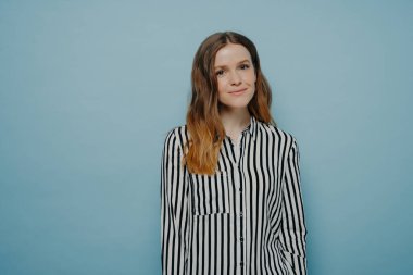 Stüdyoda gülümseyen, rahat hisseden, mutlu bir ifade takınan, stüdyoda mavi arka plana karşı poz veren genç bir kızın güzel duygular ifade ettiği bir fotoğraf.