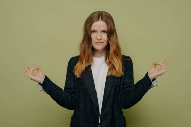 Genç ve güzel bir bayan öğrenci şık ekose ceket giyiyor ellerini Mudra jestinde tutuyor ve meditasyon yapıyor, sakin ve mutlu hissedip meditasyon yapıyor, kameraya bakıyor.