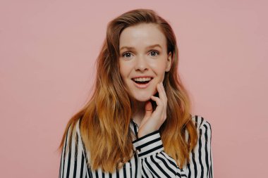 Çizgili, siyah beyaz bluzlu, orta boylu, kızıl saçlı, parlak pembe stüdyo duvarında poz verirken şaşırdığını ifade eden neşeli genç bir kadın. İnsan duyguları kavramı