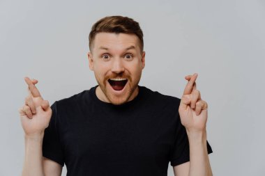 Dilek tutuyorum. Heyecanlı genç adamın portresi. Kazanma umuduyla ya da şans dileyip gri stüdyo arka planına bakarken kameraya bakıyor. Şans ve batıl inanç kavramı