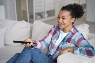 Televizyon, komedi şovu ya da film izleyen, kanepede oturan, karışık ırk kızlarına gülen. Mutlu kıkırdayan genç bayan uzaktan kumanda kullanıyor, eğleniyor, evde kanepede televizyonla vakit geçiriyor..