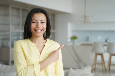 Mutlu kadın uzayı kopyalamak için parmağıyla işaret ediyor. Genç duygusal bir kadının kavramsal portresi. Reklam pankartı maketi. Evdeki oturma odasında yakışıklı Avrupalı bir kız. Dairenin modern iç mimarisi.