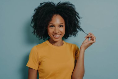 Koyu renk saçlı, güzel bir kadının stüdyo portresi neşeli bir şekilde gülümseyen, beyaz dişlerini kameraya gösteren, saçının buklesiyle oynayan, mutlu ve heyecanlı.