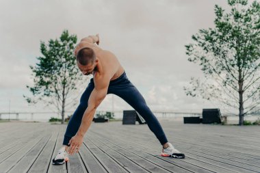 Kas sporu yapan sporcu, kardiyo antrenmanından önce vücut ısıtması yapar, açık havada poz verir, etkin bir şekilde giyinir, aktif bir hayat sürer. Spor ve spor konsepti. Mükemmel pazıları olan vücut geliştirici.