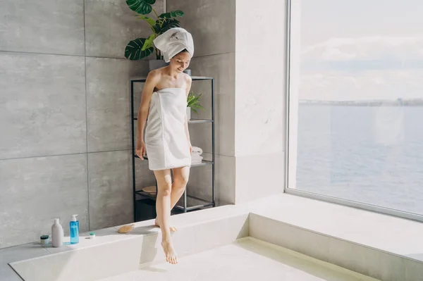 Havluya Sarılı Rahat Genç Bir Kadın Modern Güneşli Banyoda Suyla — Stok fotoğraf