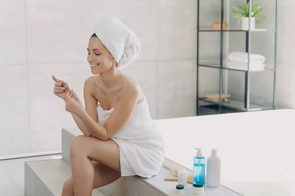 Havluya Sarılmış Gülümseyen Genç Bir Kadın Banyodaki Küvette Duran Kozmetik — Stok fotoğraf