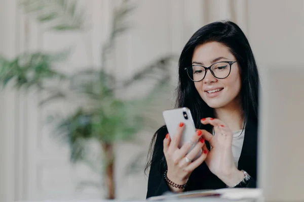 Feliz Morena Empresaria Utiliza Teléfono Inteligente Lleva Gafas Envía Mensajes — Foto de Stock