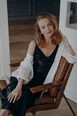 Zarif orta yaşlı kadın. Kendine güvenen şık bir bayan oturma odasındaki koltukta oturuyor. Siyah gece elbisesi ve beyaz gömlekli sarışın kadın. Mutlu beyaz kadın bir partiye gidiyor..