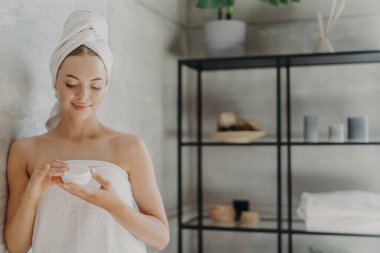 Sağlıklı ciltli memnun bir kadının yatay pozu vücut kremi sürüyor, kendine bakmak için kozmetik ürünler kullanıyor, kaplıca banyosundan sonra tuvalette poz veriyor, hijyen prosedüründen geçiyor. Kozmetoloji kavramı