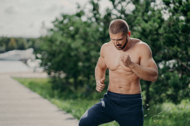 Aktif sakallı adamın yatay çekimi açık havada aktif egzersizler yapar çıplak gövde kaslı vücudu yeşil ağaçlara karşı kulaklıkla müzik dinler. Spor ve motivasyon kavramı
