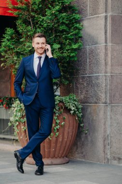 Çekici bir yönetici yöneticiye telefon eder, modern bir cep telefonu tutar, müşteriyle konuşur, resmi takım elbise giyer, bacak bacak üstüne atar, mutlu bir ifadesi vardır. İnsanlar, iş ve teknoloji kavramı